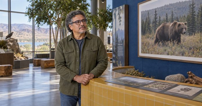 Man with navy glasses beside a framed bear photograph in a nature-centre exhibit.