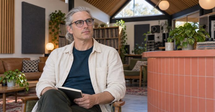 Man holding a notebook in a studio lounge beside a coral tiled counter.