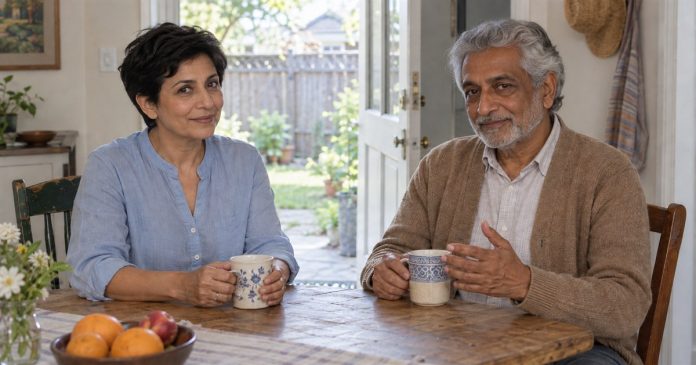 Two mature adults in conversation at a simple home table beside an open door to the yard.