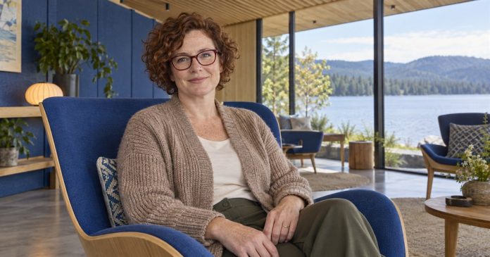 Woman with auburn curls and burgundy glasses seated comfortably in a lakeside lounge